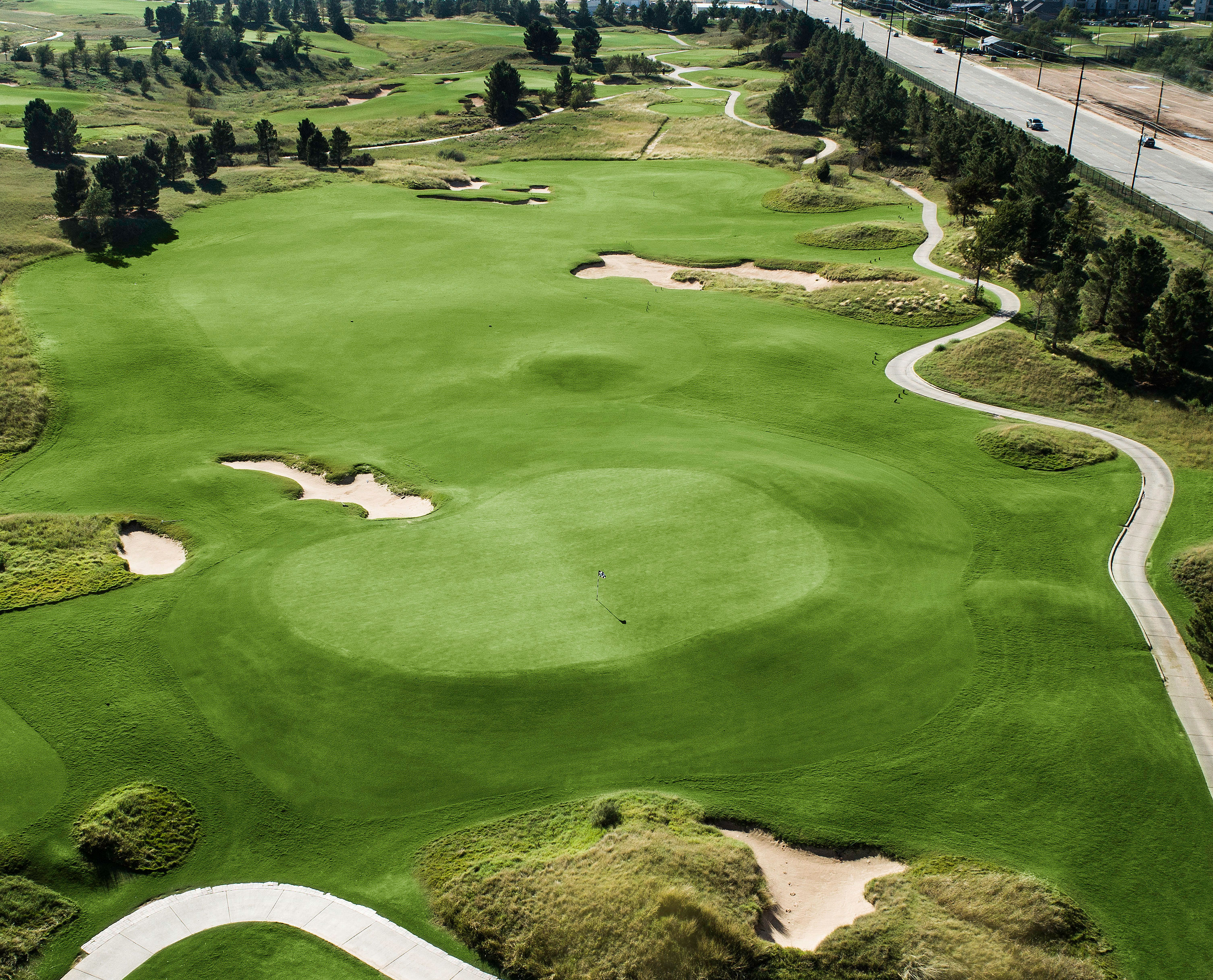 A view of a golf hole with a green fairway, trees lining the course, and a clear sky overhead.